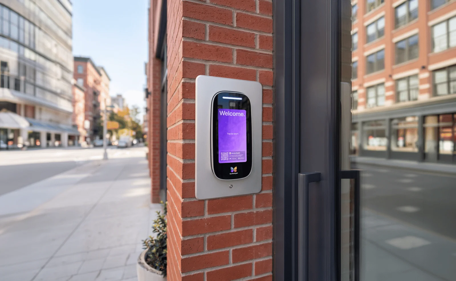 ButterflyMX video intercom panel set into a brick wall beside a building entrance